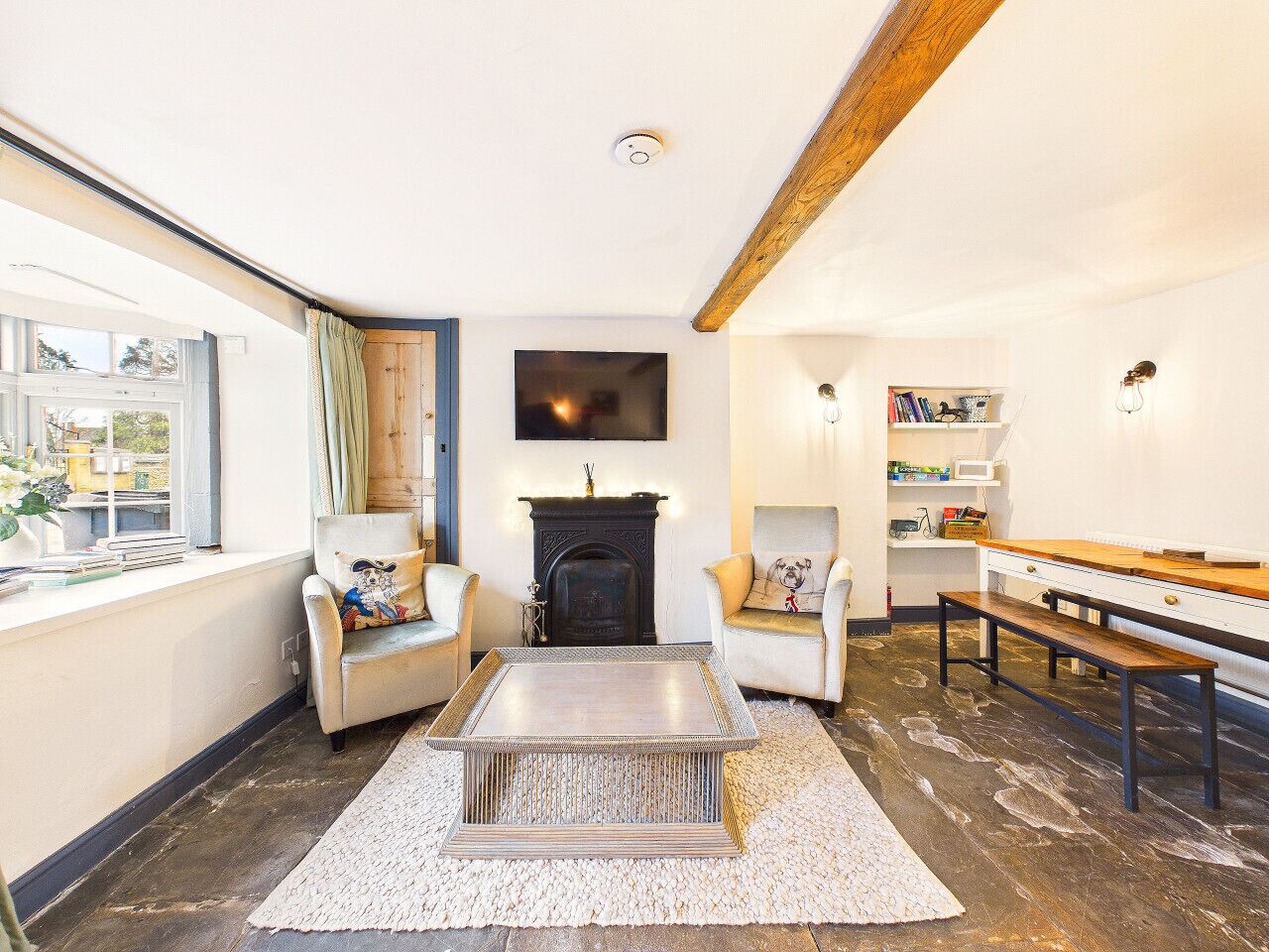 Een woonkamer met een open haard, twee fauteuils, een salontafel, een houten bankje en een boekenkast.