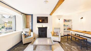 Een woonkamer met een open haard, twee fauteuils, een salontafel, een houten bankje en een boekenkast.