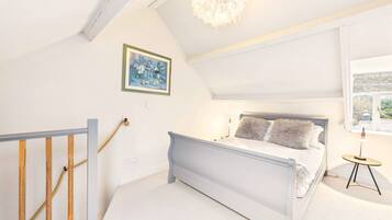A bedroom with a bed, a small table, a painting, and a window.