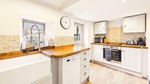 A modern kitchen with white cabinetry, a wooden countertop, a built-in oven, and a clock on the wall. - Cosy Cottage in Moreton-in-Marsh (Gloucestershire)