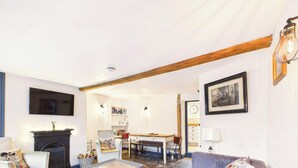 A living room with a fireplace, a dining area, and a kitchen in the background. - Cosy Cottage in Moreton-in-Marsh (Gloucestershire)