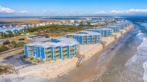 A beachfront hotel with multiple blue buildings, sandy beach access, and ocean views. - Captain's Quarters | Oceanfront Condo (North Topsail Beach)