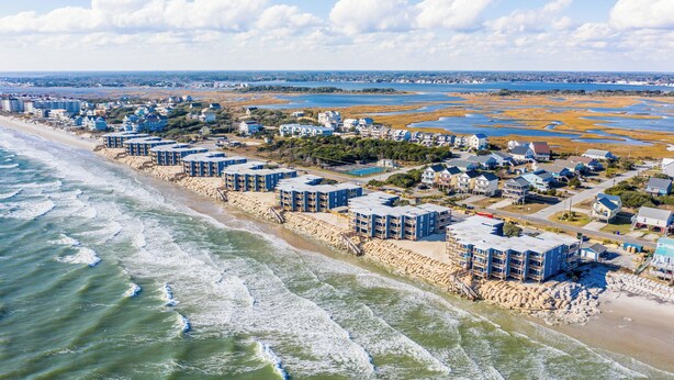 A coastal hotel with multiple buildings along the beachfront, featuring a sandy beach and ocean views. - Captain's Quarters | Oceanfront Condo (North Topsail Beach)