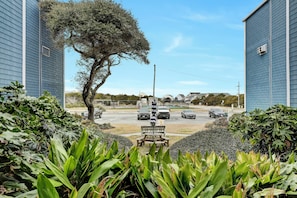Blick auf einen Parkplatz mit einer Bank und einem Baum im Vordergrund, umgeben von Grün.