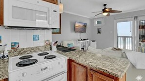 A kitchen with a white stove, wooden cabinets, and a granite countertop. - Captain's Quarters | Oceanfront Condo (North Topsail Beach)