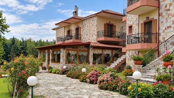A two-story stone building with balconies, a stone pathway, and a garden with flowers.
