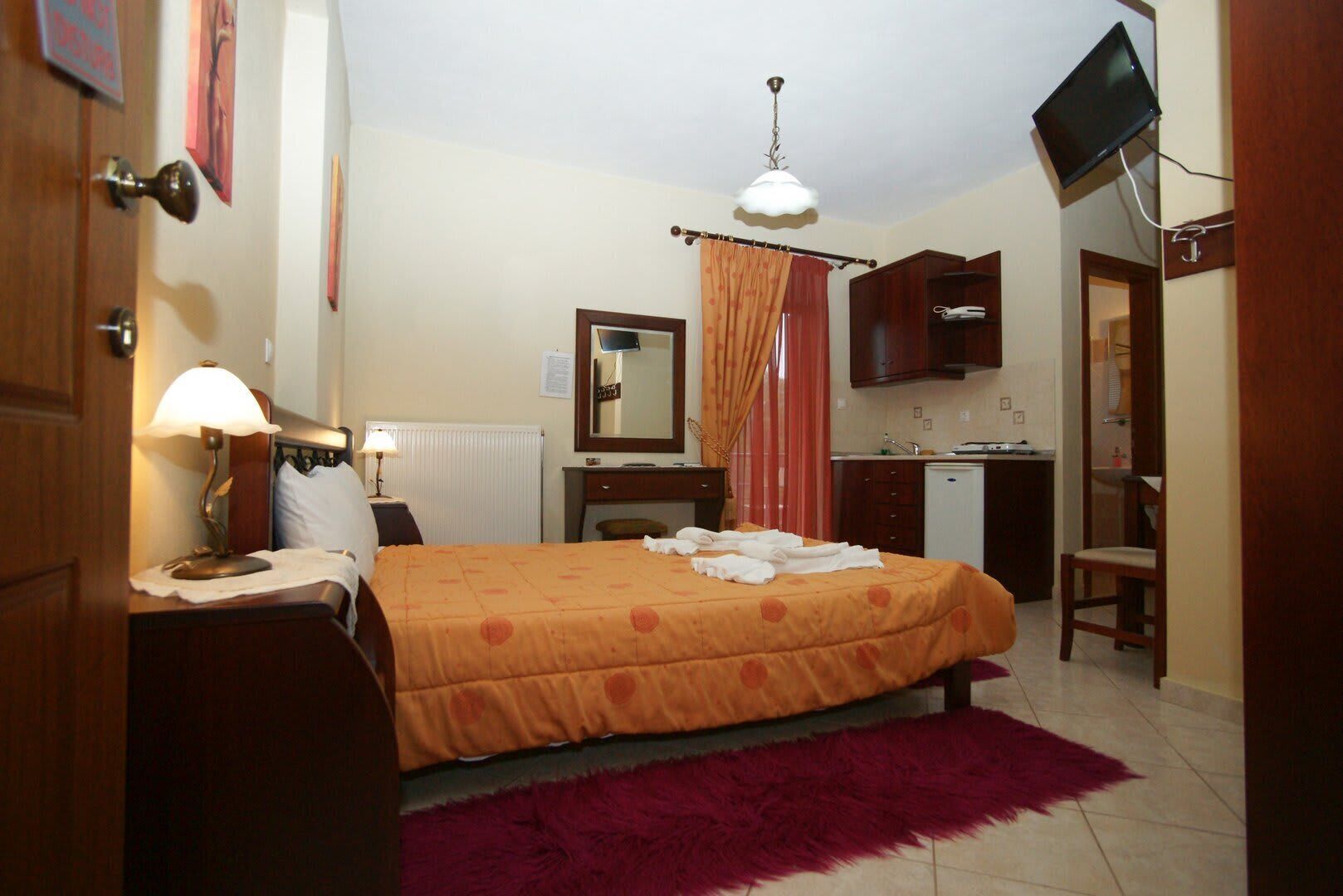 Quarto de hotel com cama, escrivaninha, cadeira, televisão e banheiro.