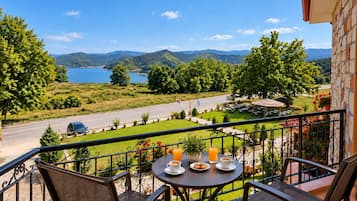 A balcony with a table set for two, overlooking a scenic landscape with a lake and mountains.