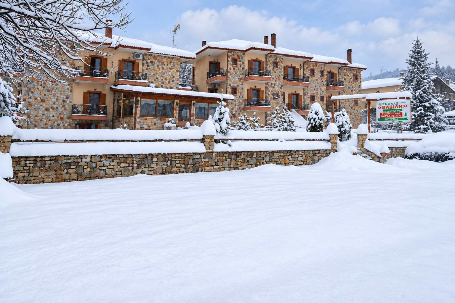 Ein mehrstöckiges Hotel mit Steinwänden und Balkonen, umgeben von schneebedeckten Bäumen und blauem Himmel.