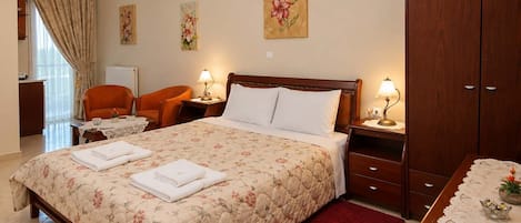 Une chambre d’hôtel avec un grand lit, deux tables de chevet avec des lampes, une armoire en bois, un tapis rouge et des œuvres d’art florales accrochées aux murs.