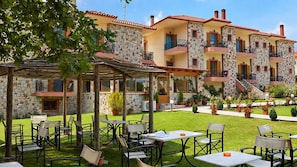 A courtyard with outdoor seating and a stone building with multiple balconies. - Orama Hotel - Lake Plastira Fireplace Family Suite (Kryoneri)