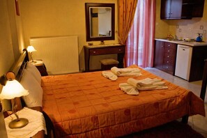 Ein Hotelzimmer mit einem Bett, einem Nachttisch, einer Lampe, einem Spiegel, einer Kommode, einem Waschbecken und einem Fenster mit Vorhängen.