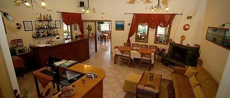 A spacious living room with a sofa, a coffee table, and a dining area with chairs and a table. There is a kitchen area with a counter and shelves.