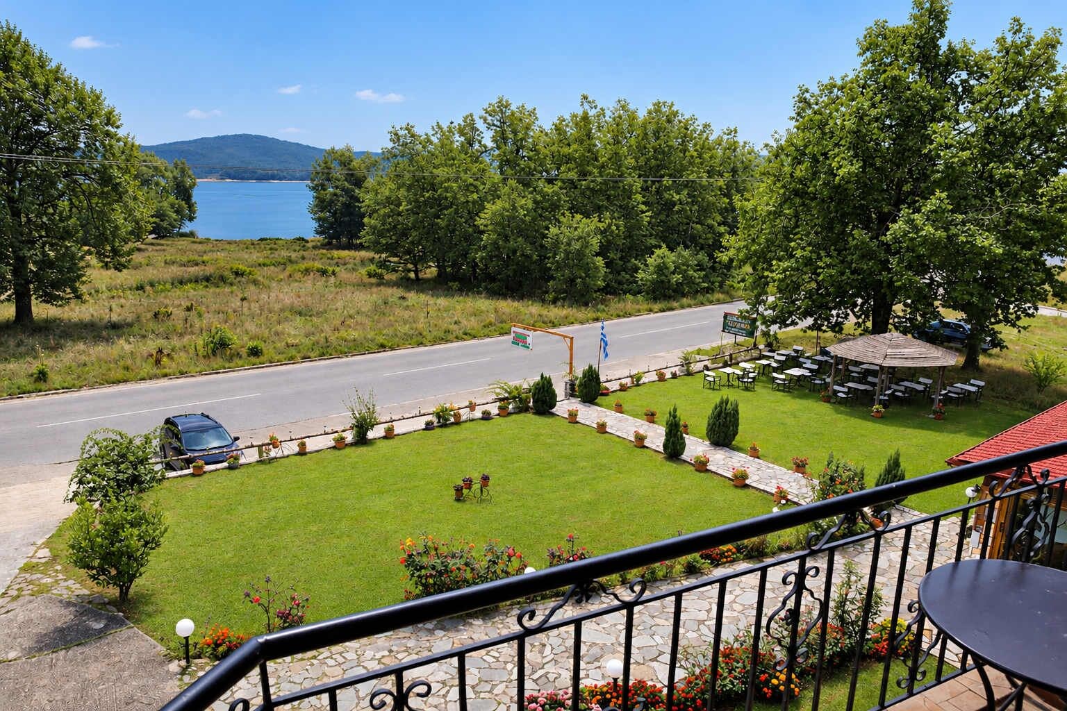 A balcony with a view of a road, a grassy area with potted plants, and a building with outdoor seating.