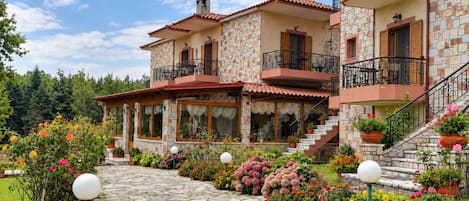 A two-story stone building with balconies, a stone pathway, and a garden with flowers.