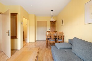 Ein Zimmer mit Holzboden, einem grauen Sofa, einem Esstisch mit Stühlen und einer Holztür.