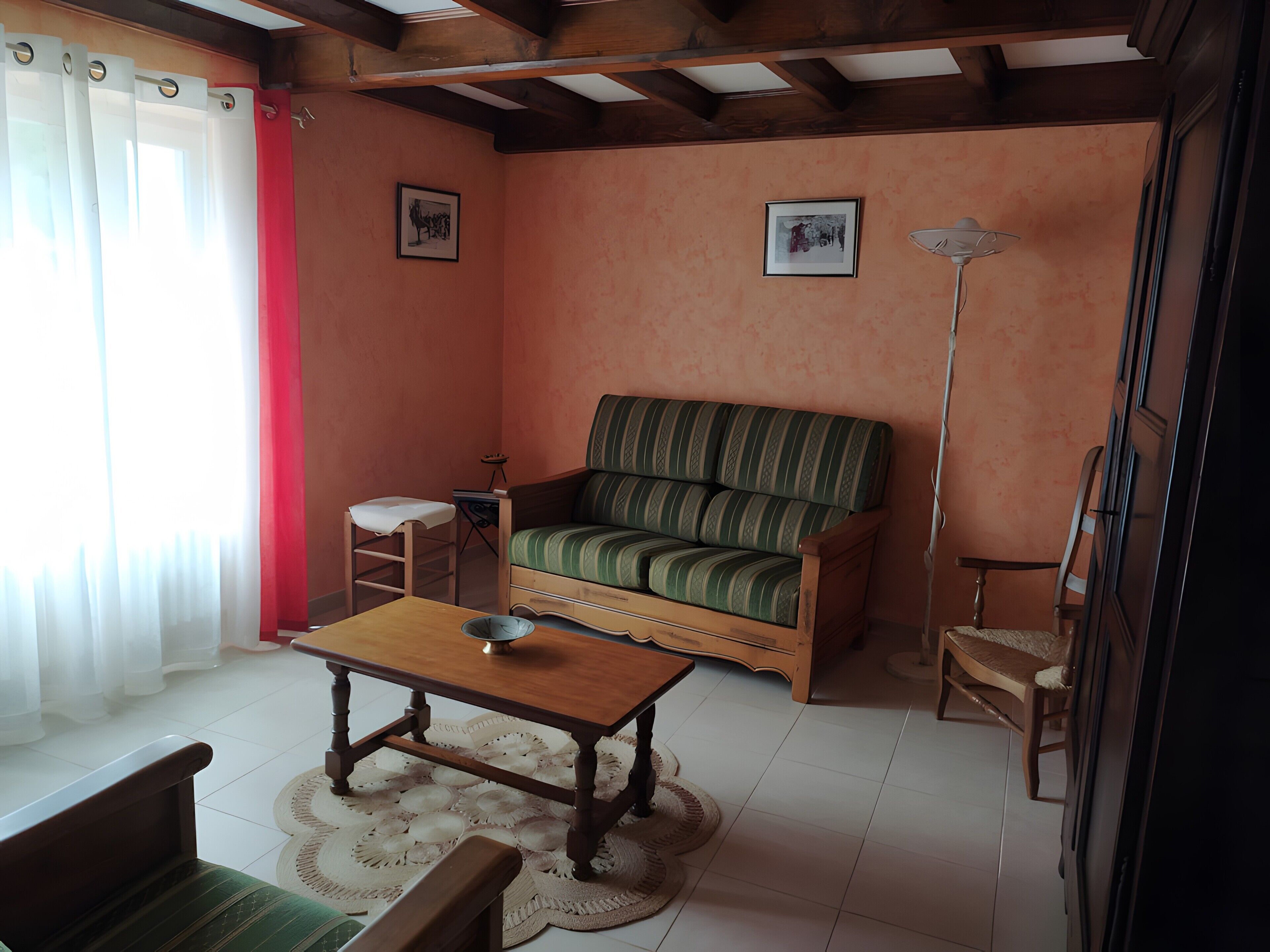 A living room with a sofa, a wooden table, a chair, a floor lamp, and a small stool.