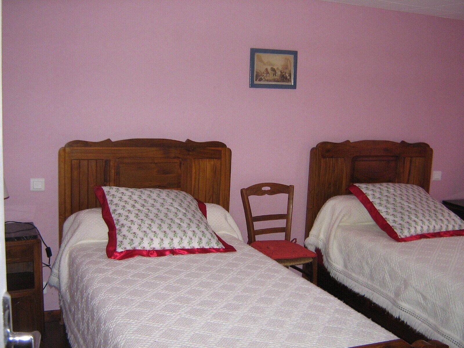 Deux lits simples avec des têtes de lit en bois, une petite chaise en bois et un tableau encadré au mur.