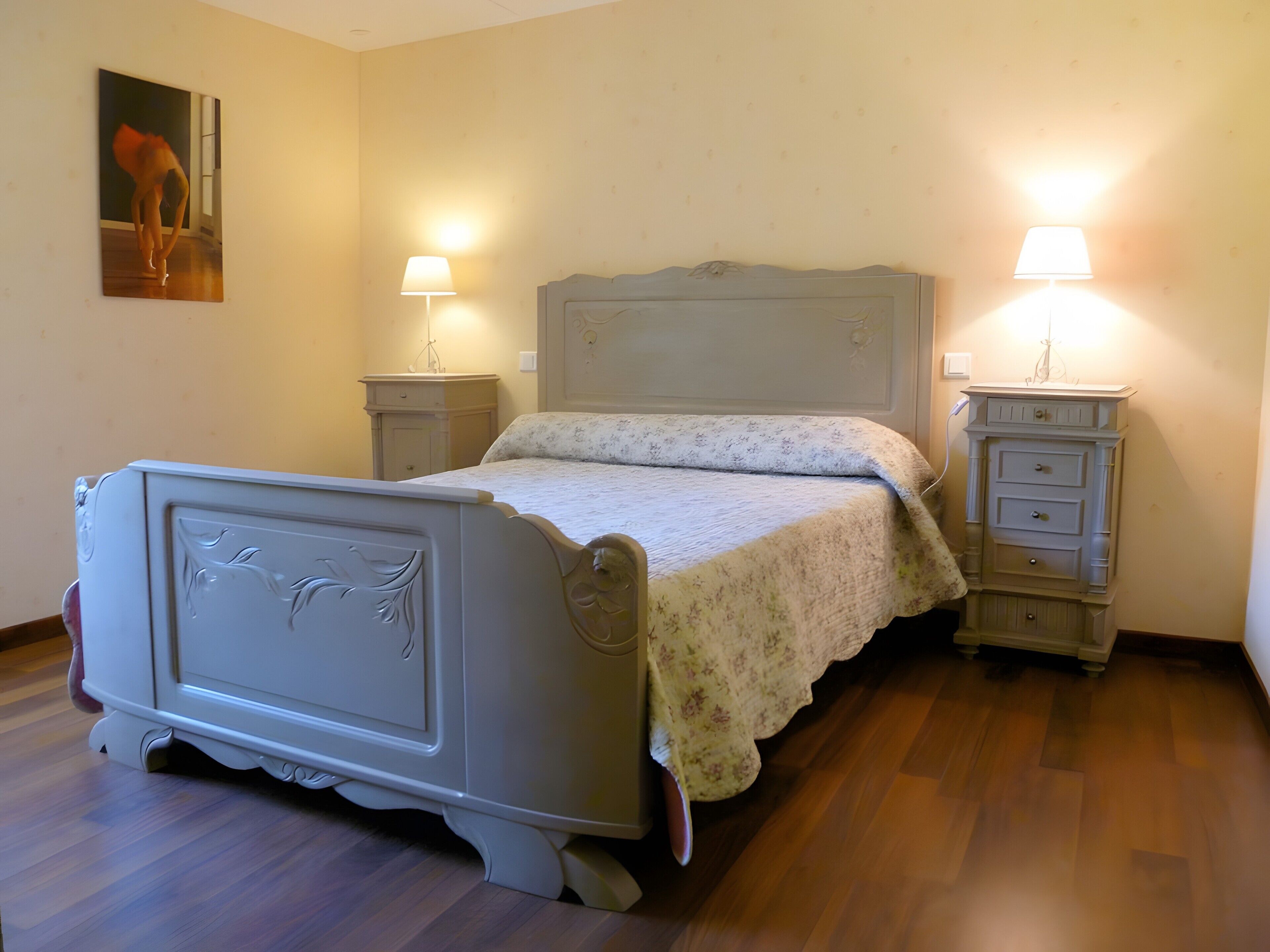 A bedroom with a bed, two bedside tables, a nightstand, a dresser, and a painting on the wall.