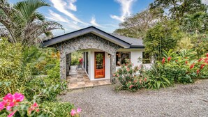 A stone-arched entrance to a house with a red door, surrounded by lush greenery and flowering plants.