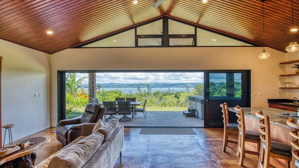 Amplia sala de estar con un gran ventanal con vistas a un paisaje pintoresco, un rincón de estar acogedor y una cocina con detalles de madera.