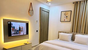 A hotel room with a bed, a TV mounted on the wall, a bedside table, and a door.