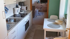 Une cuisine compacte avec des meubles blancs, un four à micro-ondes, une bouilloire et un coin repas comprenant une table et des chaises.