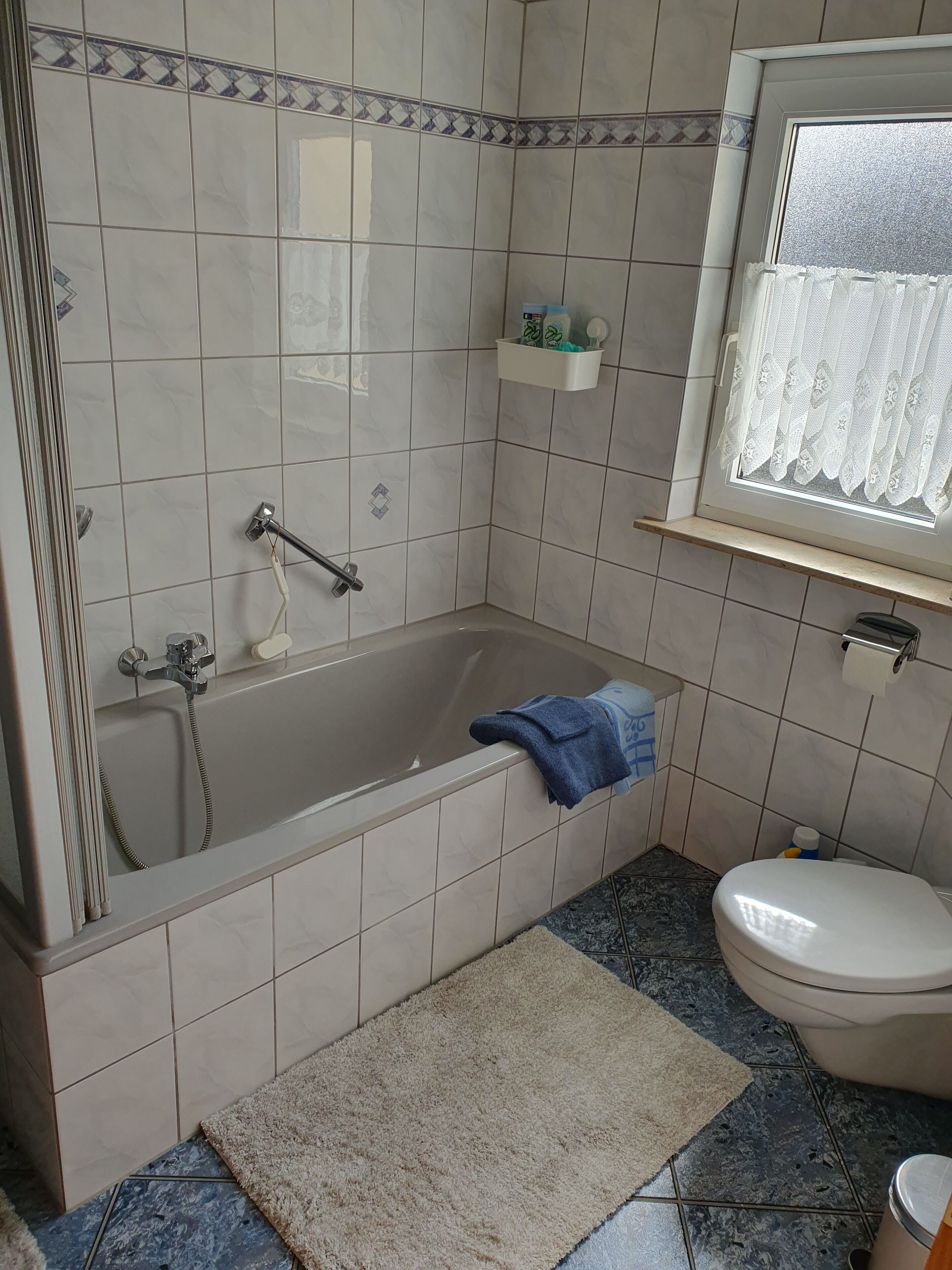 A bathroom with a bathtub, toilet, and a window with a lace curtain.