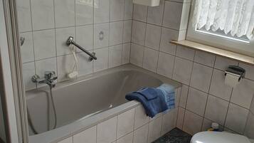 A bathroom with a bathtub, toilet, and a window with a lace curtain.