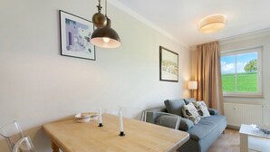 Una sala de estar moderna con una mesa de comedor de madera, un sofá y una ventana que da a un campo verde.