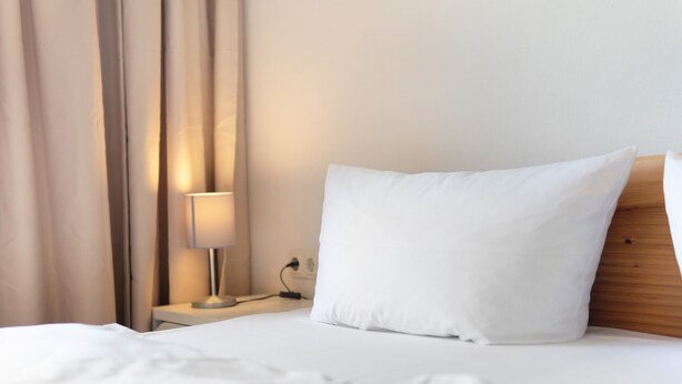 Una habitación de hotel con cama, mesita de noche, lámpara y cabecero de madera.