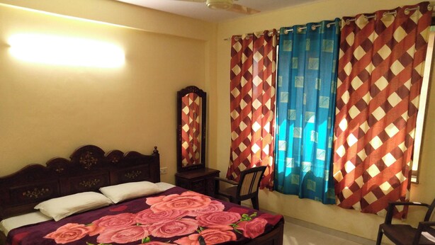 Une chambre à coucher avec un lit, une commode, une chaise et des rideaux.