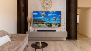 A modern living room with a large flat-screen TV mounted on a white console, a beige sofa, and a wooden floor. - Solitude in Ružići - Istrien / Solitude in Ružići - Appartement für 4 Personen (Ružići)