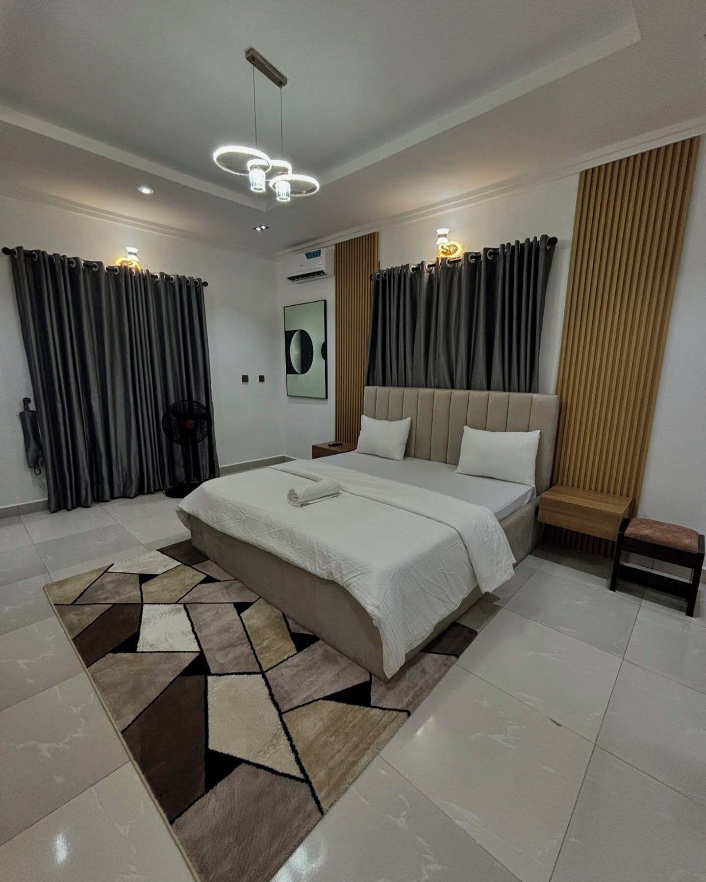 A modern bedroom with a large bed, a bedside table, a floor lamp, and a wall-mounted air conditioner.