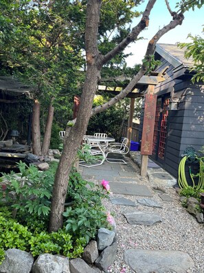 A garden with a stone pathway, a wooden pergola, and a table with chairs.