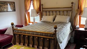 Un dormitorio ordenado con cama, un banco tapizado en verde, un sofá rojo y una mesita de noche de madera con lámpara.