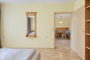 A bedroom with a bed, a wooden wardrobe, a mirror, and a dining area with a table and chairs.