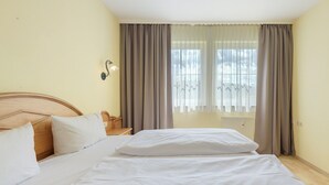 A hotel room with a large bed, a wooden headboard, a bedside table, and a window with curtains. - Superior Apartment with Dog – Lake View, Balcony, Self Check-in (Spalt)