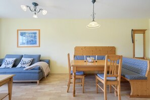 A room with a wooden dining table, blue upholstered chairs, a wooden bench, a sofa, and a framed picture on the wall.