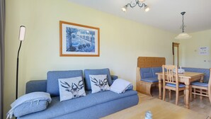 A living room with a sofa, a dining table, chairs, a lamp, and a framed picture on the wall. - Superior Apartment with Dog – Lake View, Balcony, Self Check-in (Spalt)