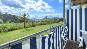 Ein Balkon mit Blick auf eine Rasenfläche und Bäume, einem Metallgeländer und einem Holzboden.