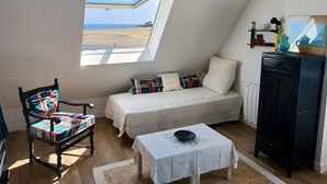 Ein Schlafzimmer mit Bett, Stuhl, Nachttisch, Schrank und Fenster mit Blick auf den Strand.