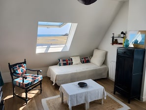 Een slaapkamer met een bed, een stoel, een klein tafeltje, een kast en een raam met uitzicht op het strand.