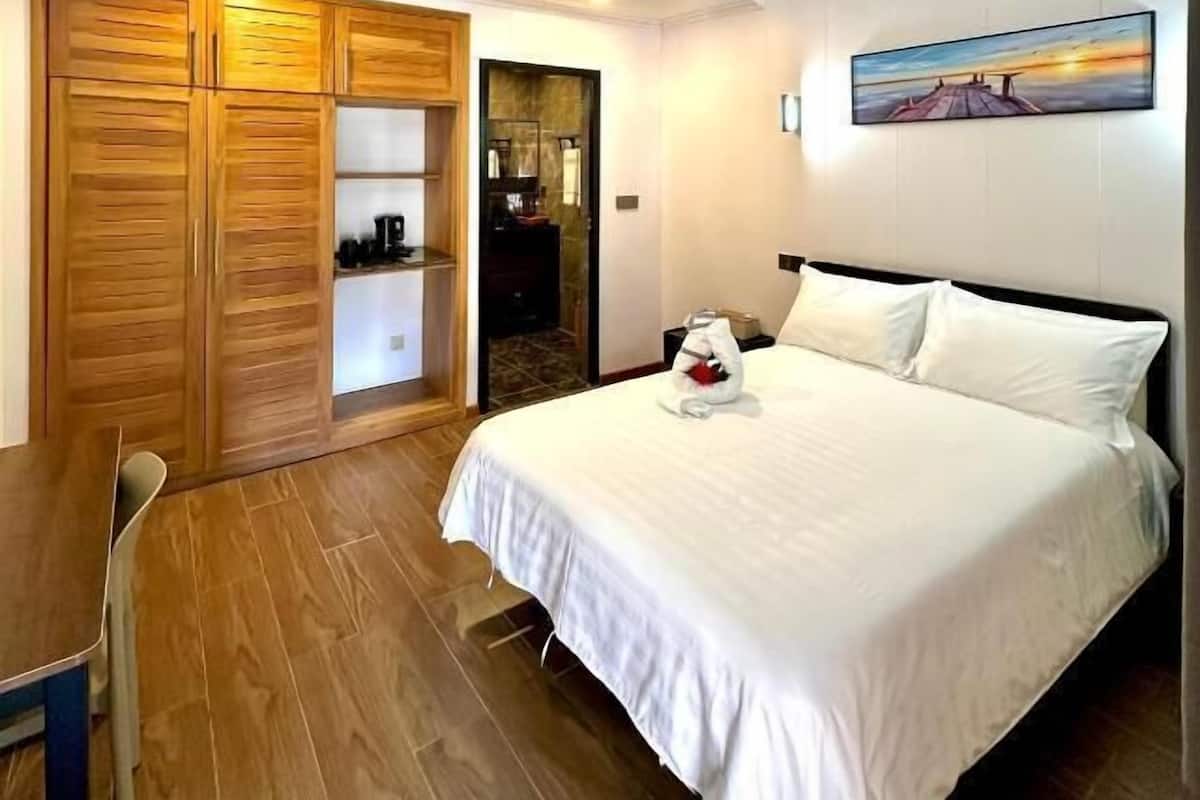 A hotel room with a bed, a wooden wardrobe, a desk, and a painting on the wall.