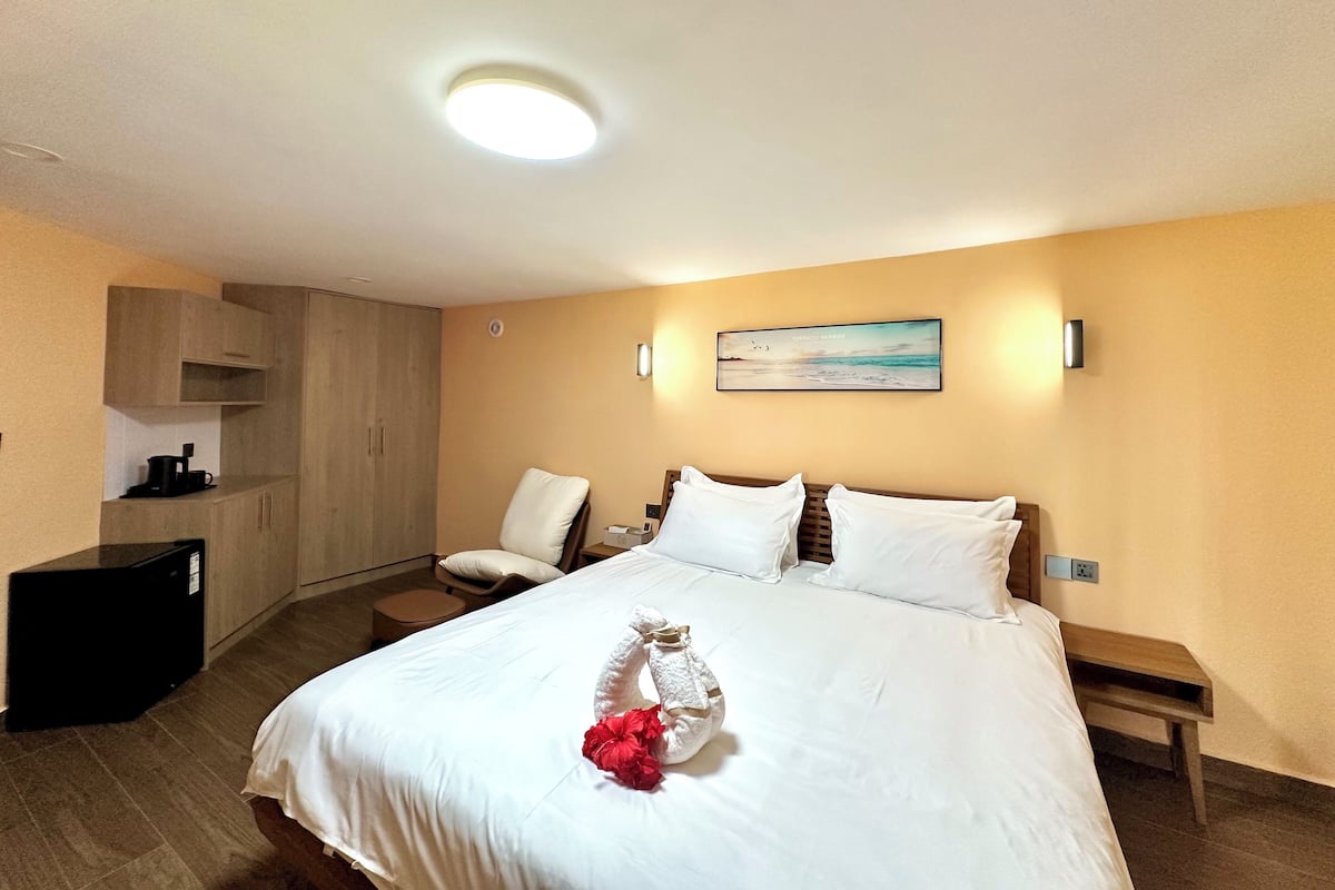 A hotel room with a bed, a desk, a chair, a wardrobe, and a painting on the wall.