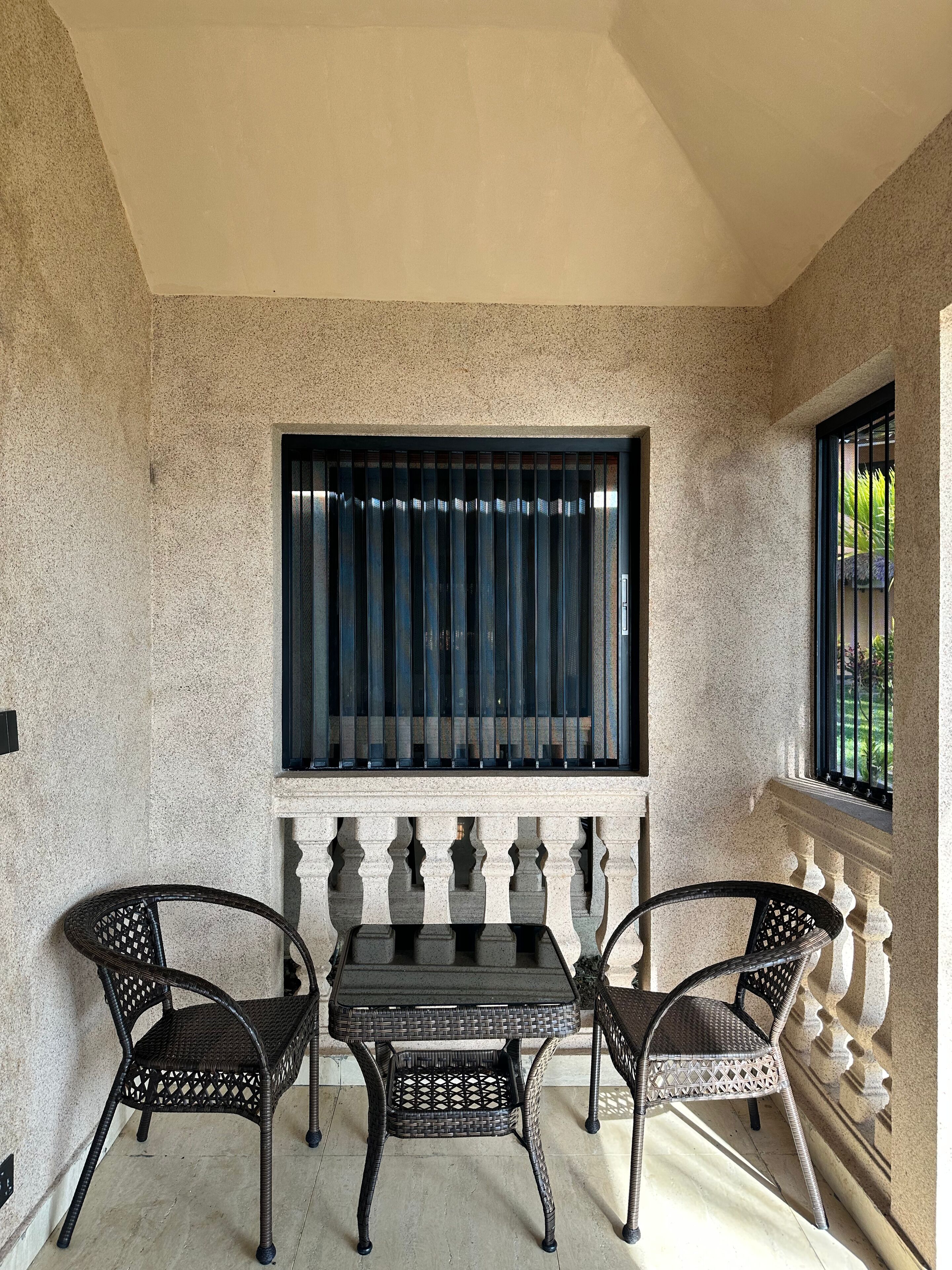 A balcony with a table and two chairs, a window with bars, and a view of greenery.