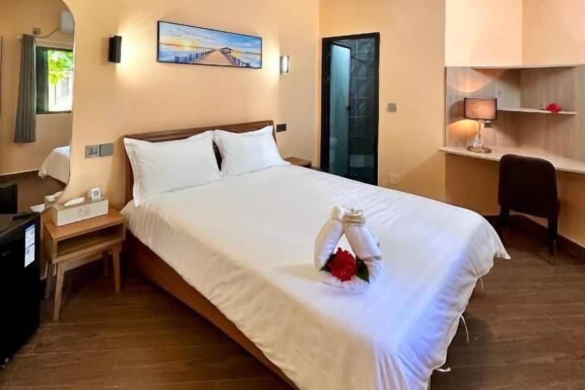 A hotel room with a large bed, a desk, a chair, and a painting on the wall.