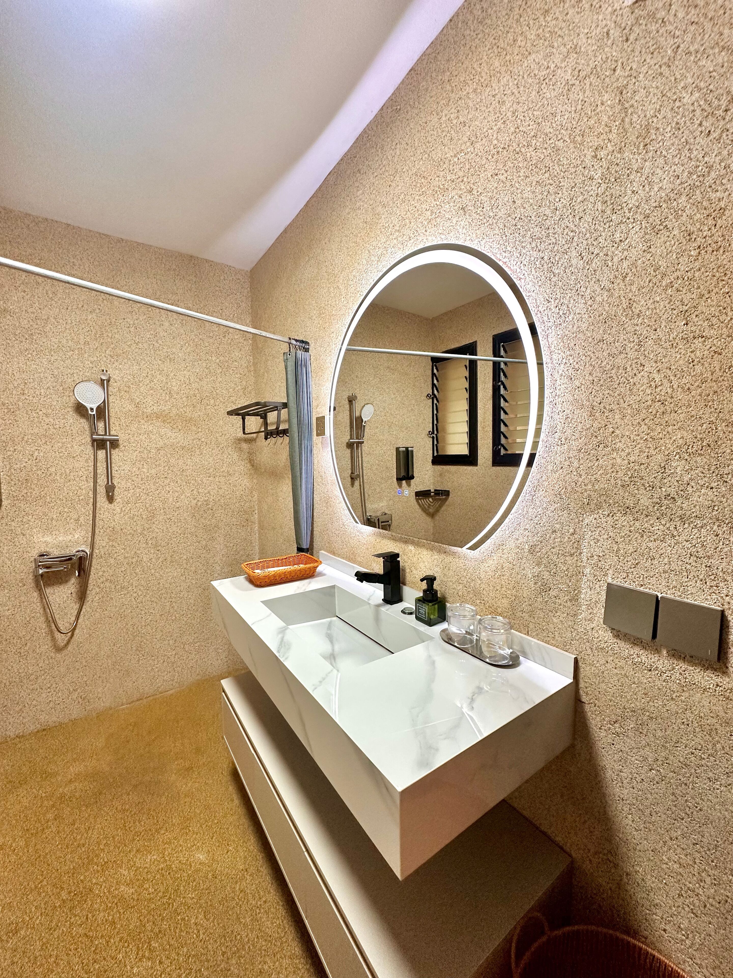 Een moderne badkamer met een wit wastafelmeubel, een ronde spiegel, een handdouche en een handdoekrek.