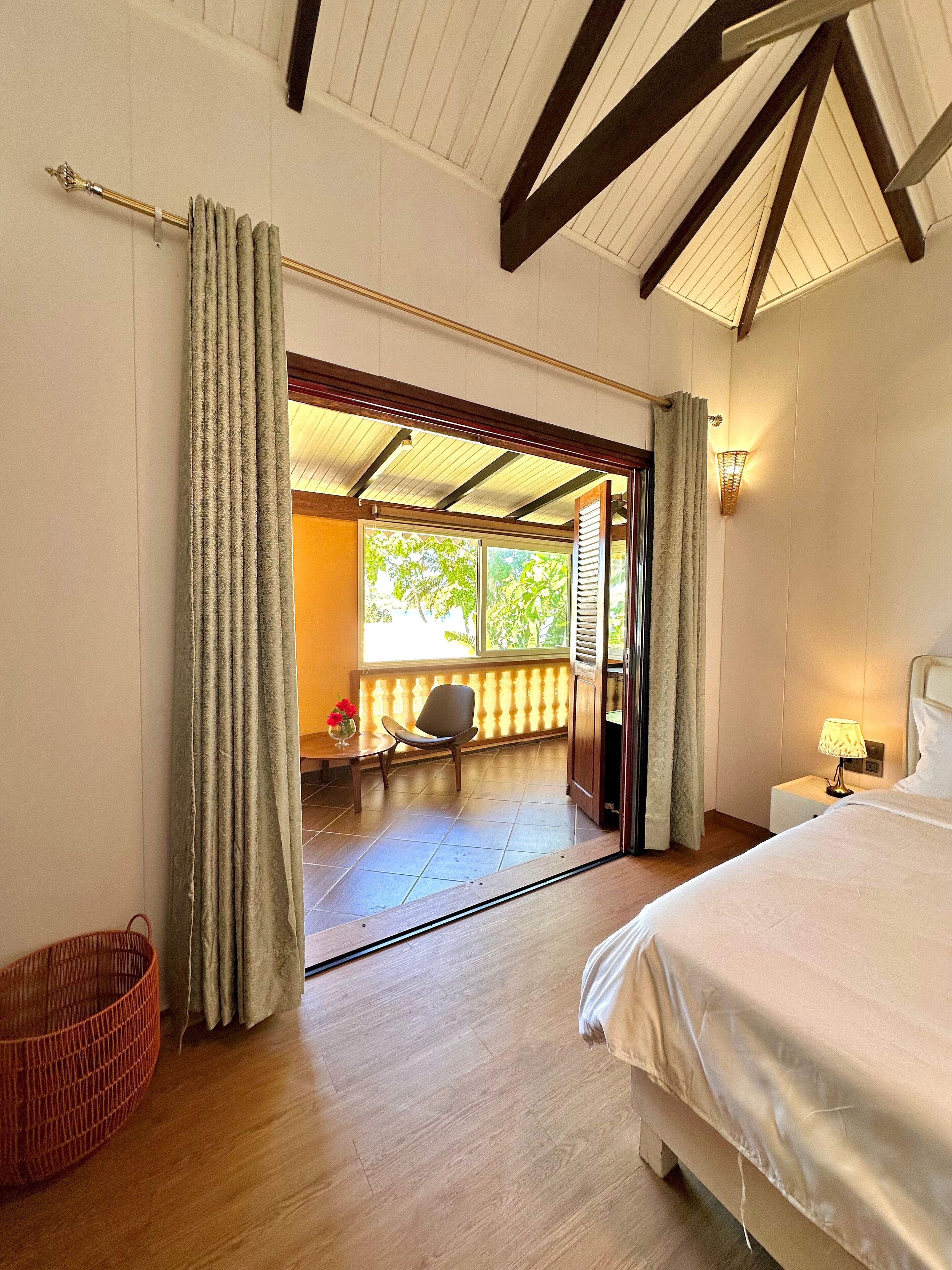 A hotel room with a bed, a chair, a small table with flowers, and a view of the outside.