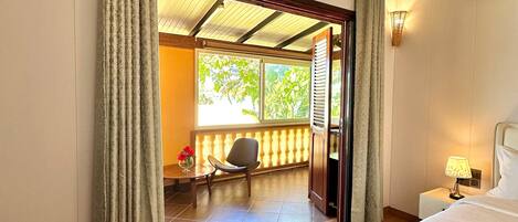 A hotel room with a bed, a chair, a small table with flowers, and a view of the outside.